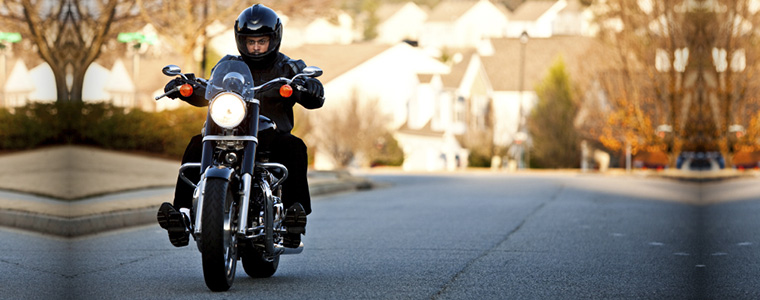 Hispanic male riding motorcycle on residential street with houses in the background to illustrate whether you need motorcycle insurance in albany if you have auto insurance