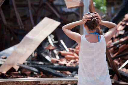 Back shot of woman with hands on her head surprised as she sees her house destroyed after an earthquake
