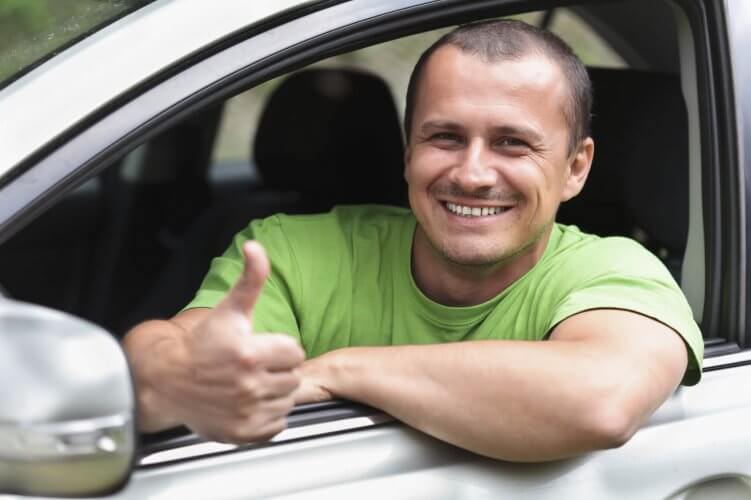 Happy young man with new car smiling in front seat with thumb up gesture.