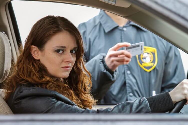 Concerned young woman pulled over by cop for drinking and driving. Policeman holding her license in background to illustrate why it is better not to drink and drive
