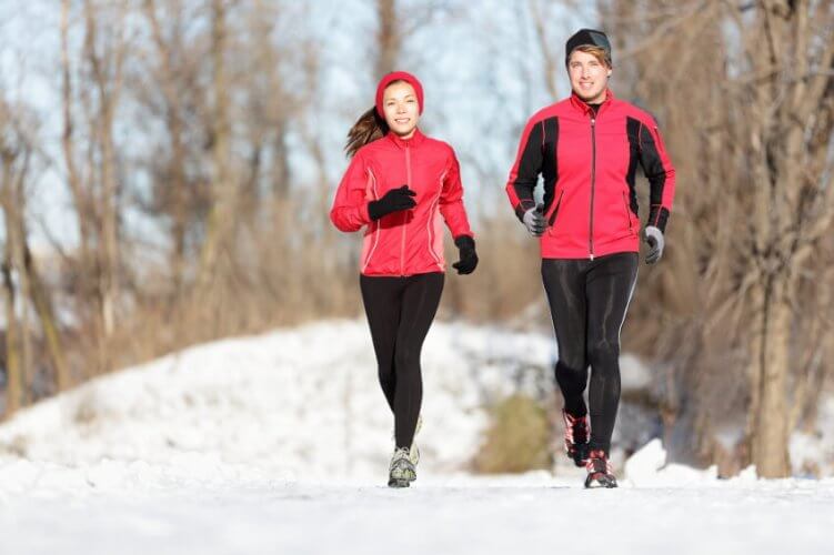 A Caucasian couple jogging in the woods to illustrate running in winter.