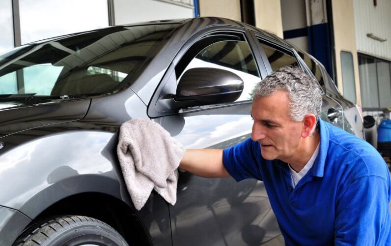 Older man cleaning and giving finishing touches to a car as part of its maintenance.
