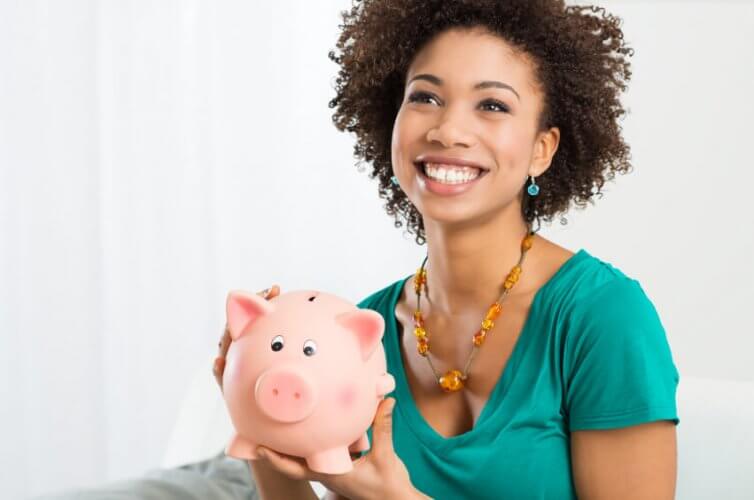 Happy young black woman holding a piggy bank to illustrate savings