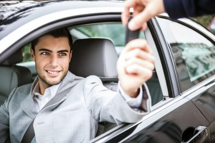 Happy young man with new car smiling in front seat getting the key from salesman.
