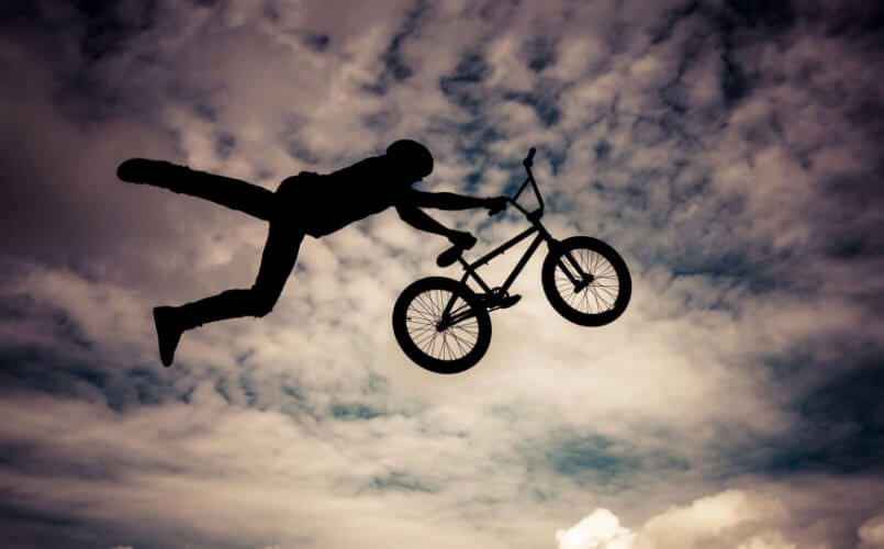 Silhouette of man with bmx bike making an extreme trick on the air with cloudy sky as background.