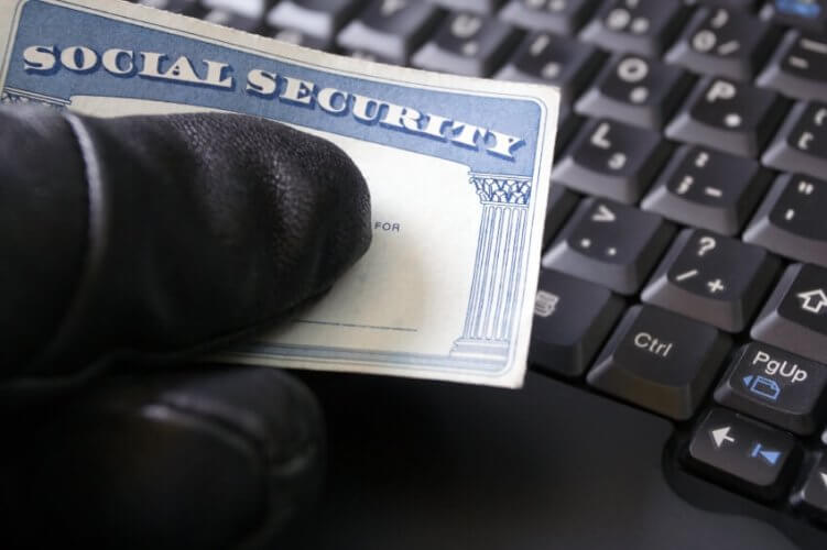 Hand in glove holding a social security card against a keyboard illustrating identity theft.