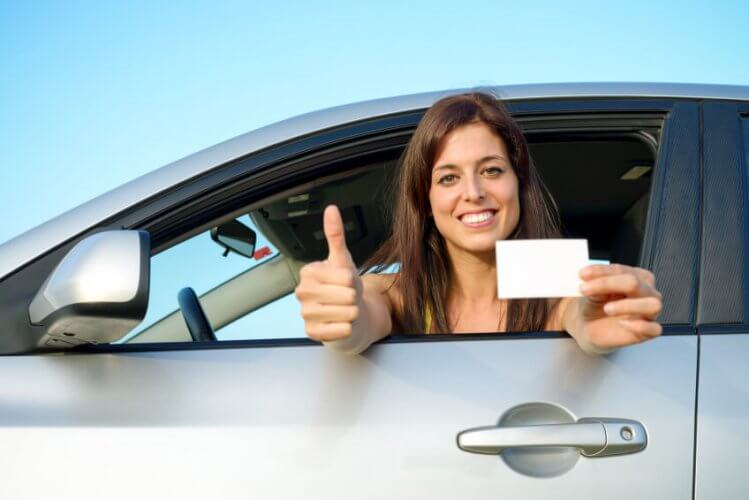 Female young car driver giving the thumbs-up after passing the driving license test showing her license