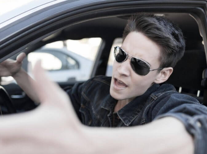 Man with sunglasses driving enraged screaming and waving his hands at another driver on the road to depict road rage