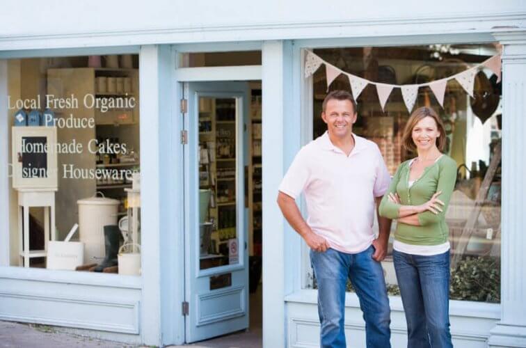 A couple smiling at door of their local business, happy because they have commercial insurance for small business
