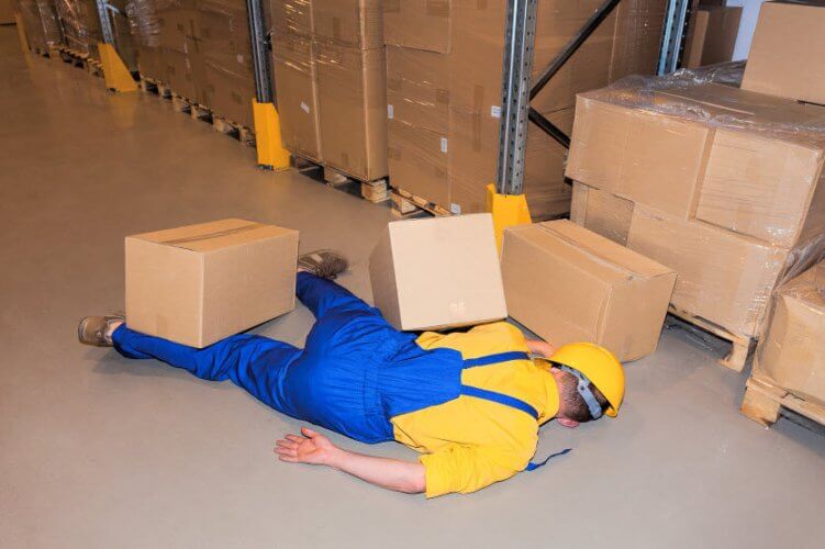 A worker lying on floor with tilted helmet and boxes over him illustrating workers injury compensation coverage