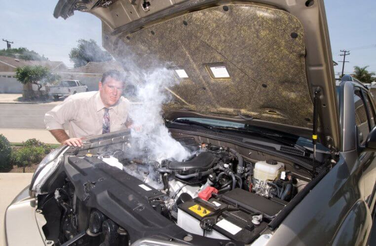 Car with opened hood with smoke coming out and a concerned man in the back to illustrate overheating in summer.