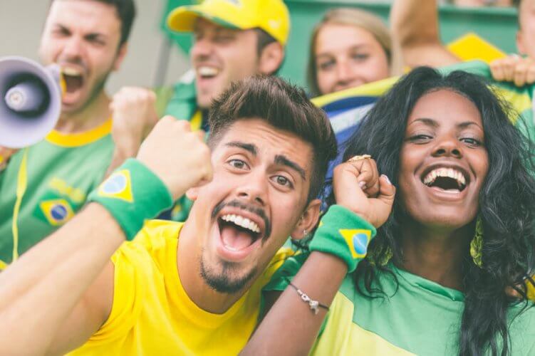 Brazilian soccer fans at a Stadium. Close up to interracial couple joyfully showing Brazil's a flag on their wristbands