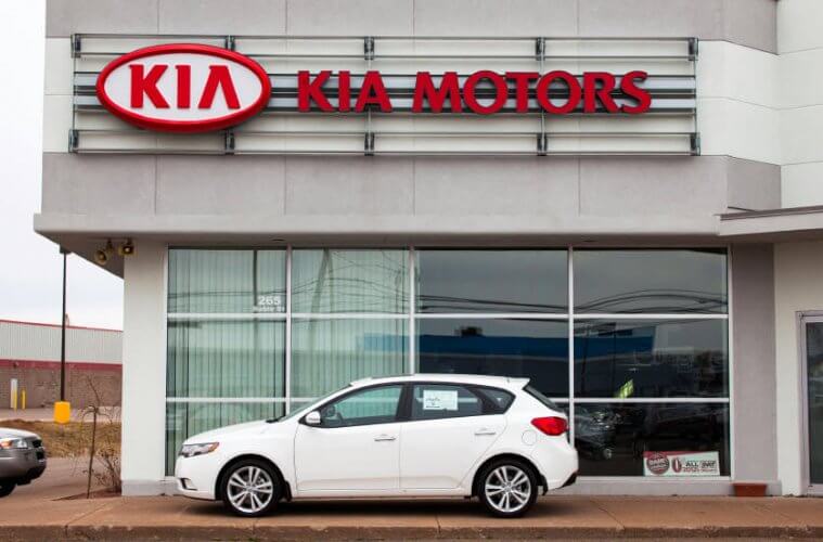 Kia Rio Hatchback parked in front of a KIA MOTORS showroom to illustrate KIA worker's comprehensive disability fraud.