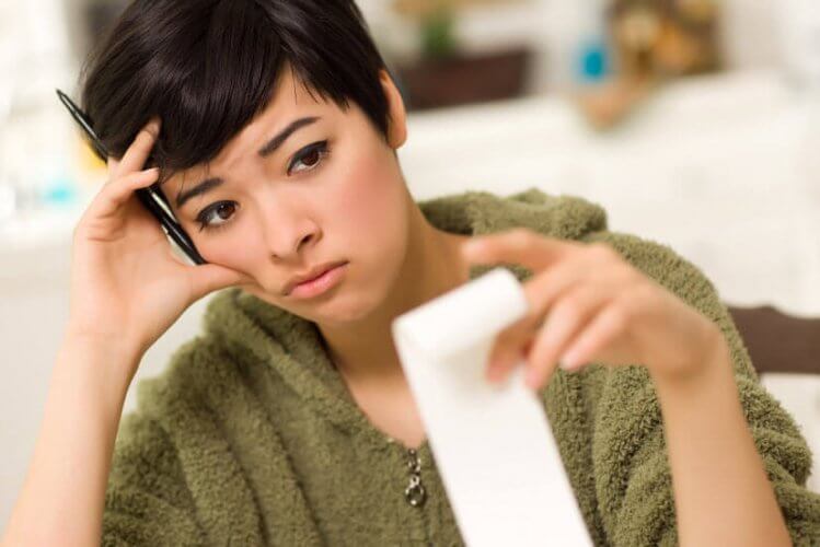 Concerned young woman with hand with pen on temple wondering how to get out of debt to depict a few tips to get out of debt.