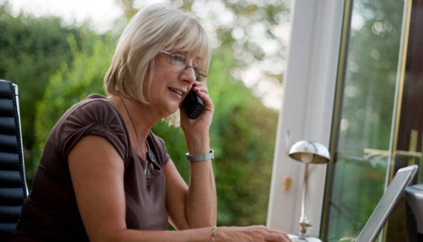 Middle-aged woman on the phone and computer in her home-based business illustrates why home-based businesses need business insurance