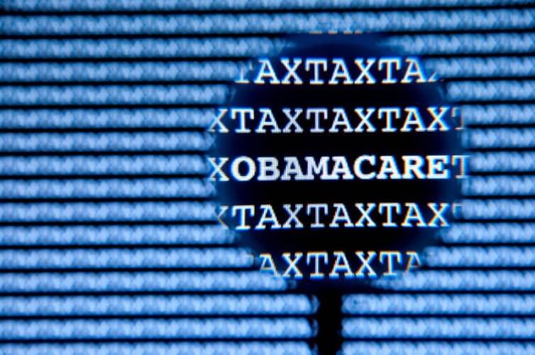 Close up to the word OBAMACARE between the word TAX repeated several times also in the blurred background to depict how Obamacare subsidies may affect your tax refund
