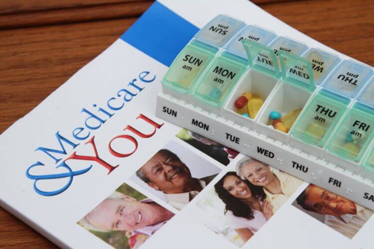 Medicare & You magazine on a wooden table with a 7 day pillbox on top. to depict potential medicare scams