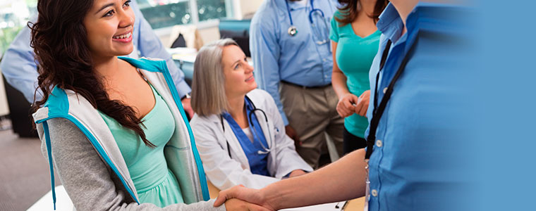 Young woman shaking hands with Insurance Agent to see if she qualifies for Medicaid. In background, doctors and other agents chatting.