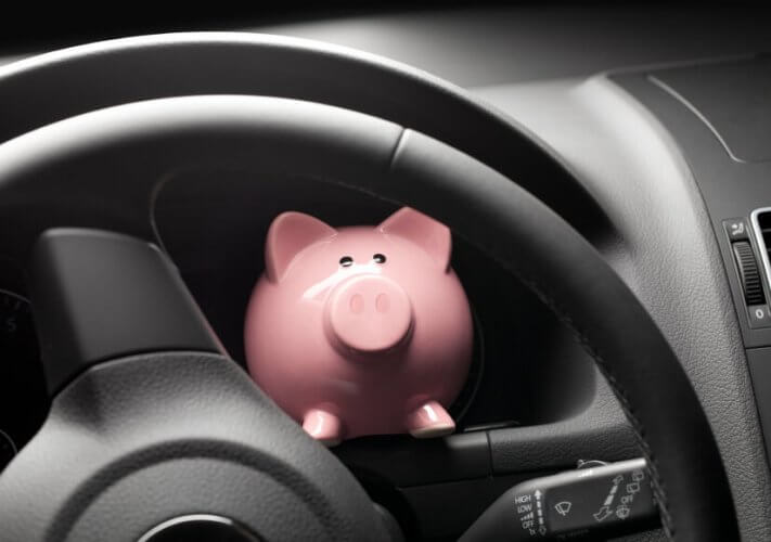 Piggy bank behind car wheel on car dashboard saving your money as an insured driver