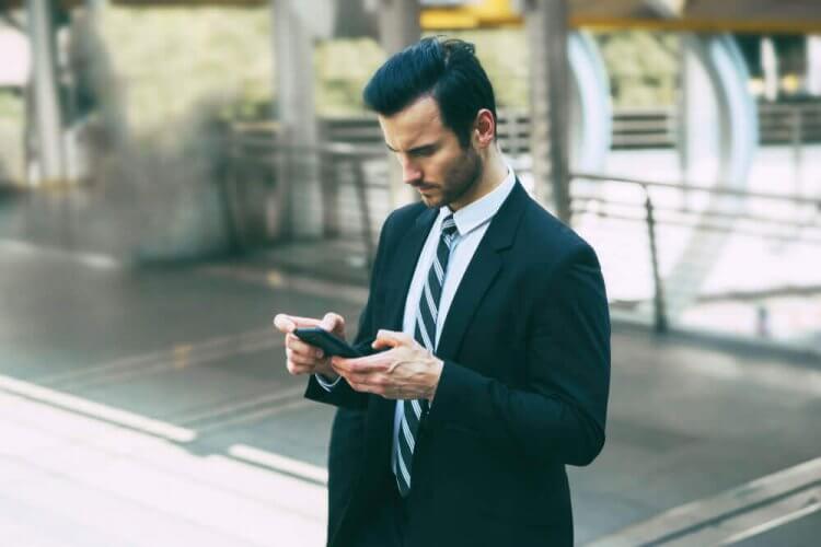 Handsome man in suit and tie looking at smartphone to showcase how a new app gives homeowner's view of burglars breaking into home