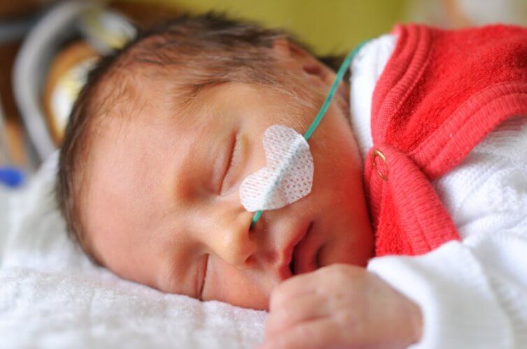 Baby with nasal probe and medical heart-shaped medical tape sleeping on hospital bed