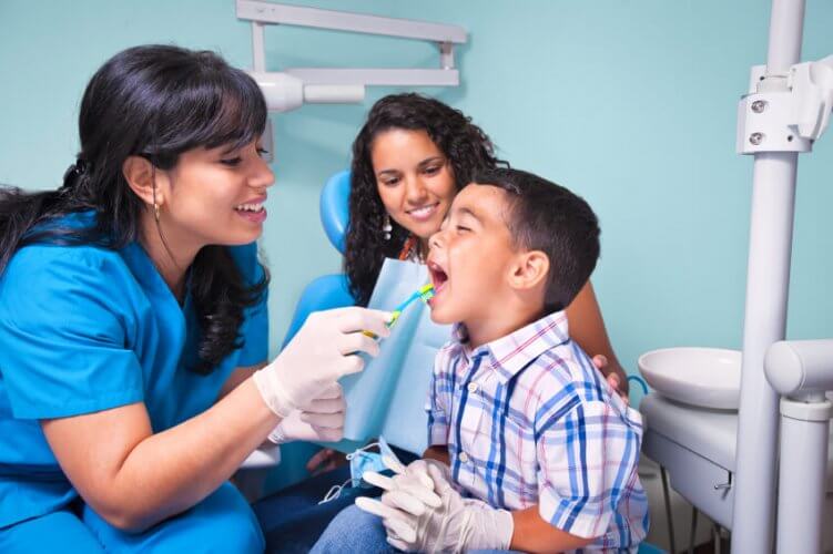 Hispanic female dentist with boy patient and his smiling mom behind him.