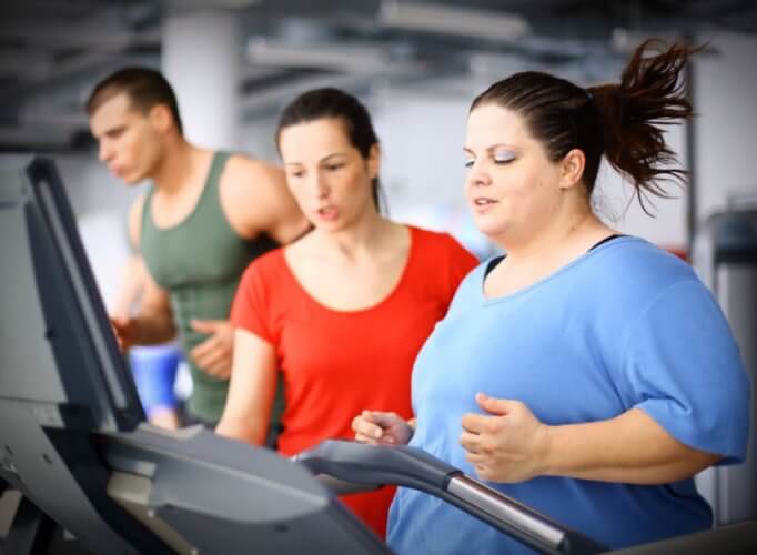 Obese woman exercising next to a slim female trainer and a fit man.