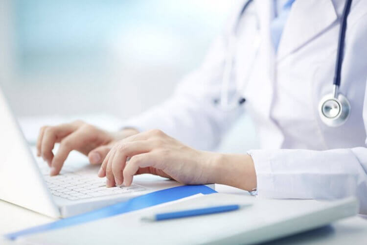 Closeup to doctor's hands working on laptop typing for patient.