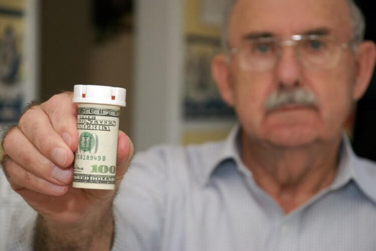 Old man showing a pillbox covered with a 100 dollar bill.