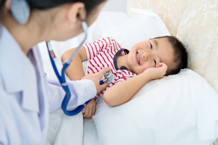 Female doctor examining a smiling kid patient lying on a hospital bed.