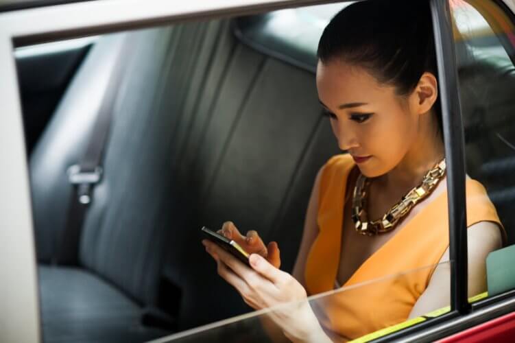 Young Asian woman texting in the backseat of a car
