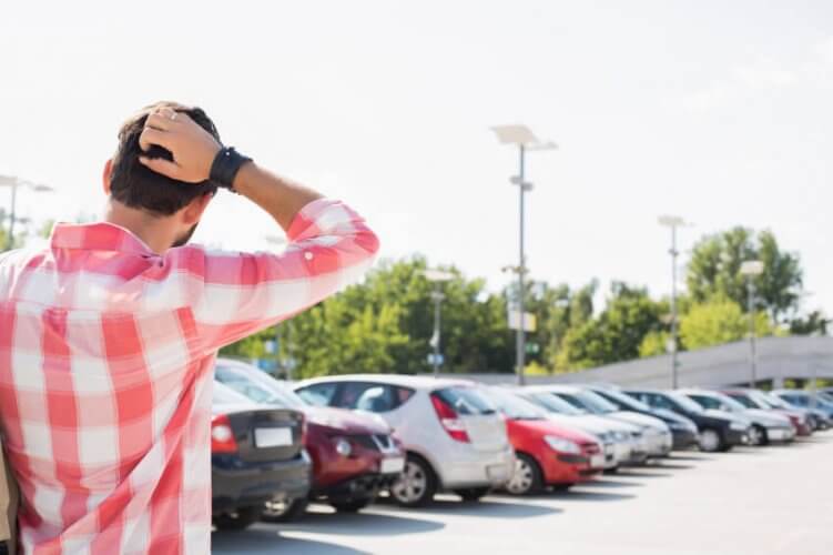 Back picture of a concerned young man with hand on head looking at a long line of cars in parking lot