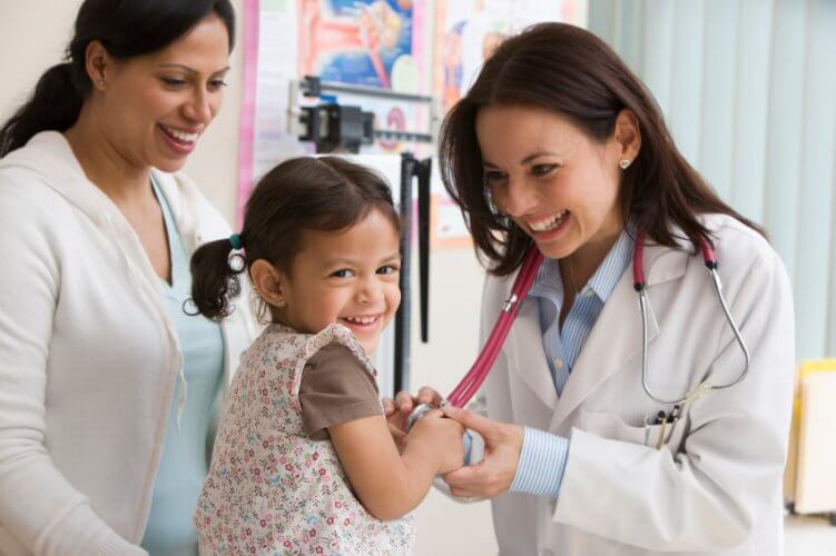 Toddler girl laughs holding the female doctor's stethoscope while the she examines her.