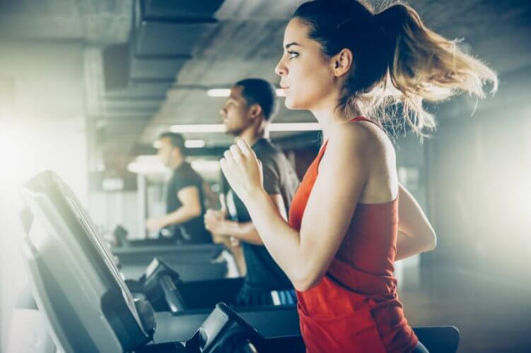 Picture of the treadmill area of a gym with fit men and a young woman