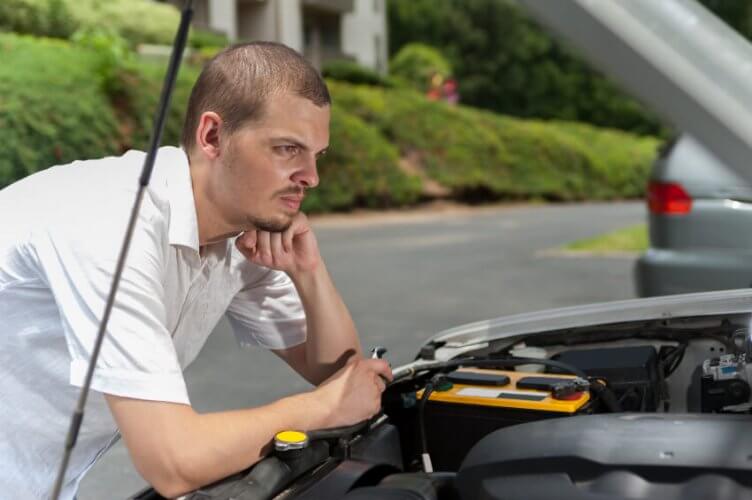 Thoughtful young man observes car's engine without knowing what to do