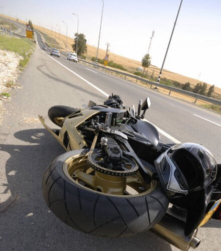 Motorcycle fallen on the side of road with driver's helmet on top. Break marks on the road.