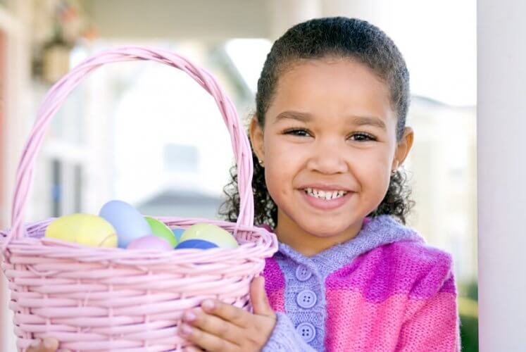 A young Latino girl holding a basket full of easter eggs.
