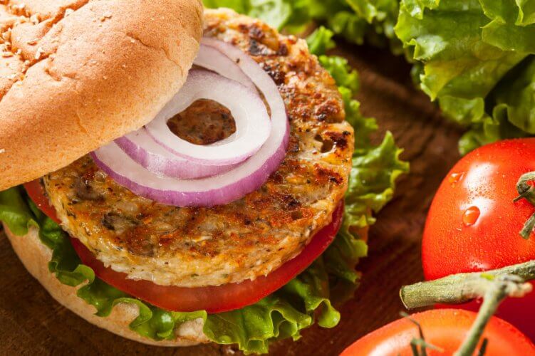 Close up of a hamburger with the top bread tilted to one side to show lettuce, tomato, grilled patty and fresh onion slices.