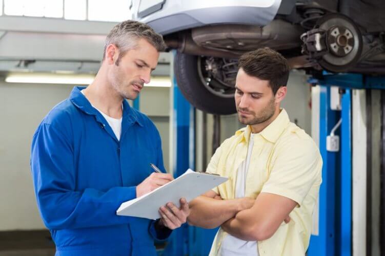 Middle aged mechanic explaining to young man the maintenance procedures performed on his car