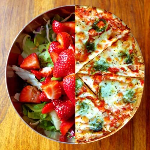 Bowl on wooden table. Half contains strawberry salad and the other half looks like half pizza.