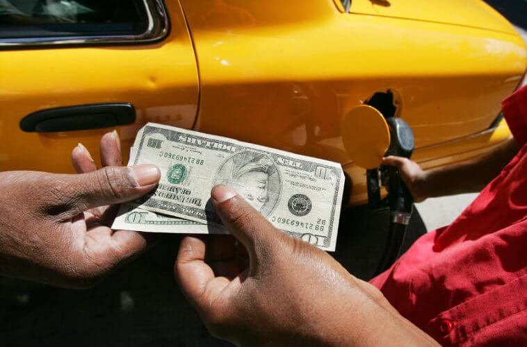 Close up to a costumer handing two 10 dollar bills to the sales man as he fills his car's tank to illustrate 6 Ways to Stay Safe at Summer Music Festivals