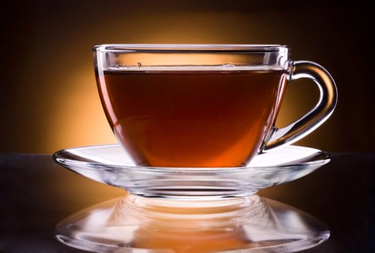 Cup of black tea in glass cup on glass plate. Reflection of the plate on the table.