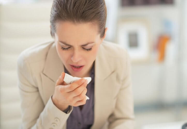 Young businesswoman coughing on a tissue on her right hand.