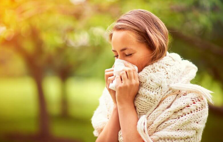 Young female in a park. She wears a scarf and is blowing her nose with a tissue.