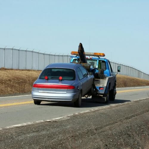 Car being towed by a car crane on an empty road.