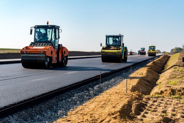 New road construction. Four Road Roller Machines are doing their job. Dust and dead grass on the side of the road.