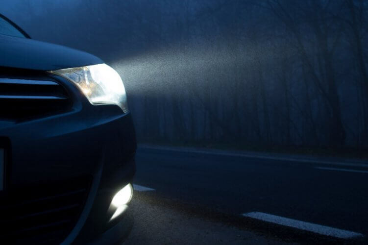 Close up to the left headlights of a car driving at night on a lonely road.