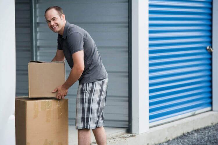 A middle aged man about to put two boxes inside a storage unit to illustrate how Will Renters or Homeowners Insurance Cover My Stuff While It’s in Storage.