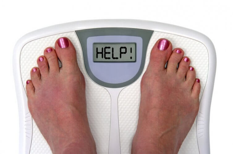Close up to woman's feet with nail polish standing on a weighing scale with the word 