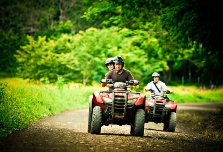 Two off-road vehicles on a trail. A couple rides one, a man rides the other. All wear helmets.